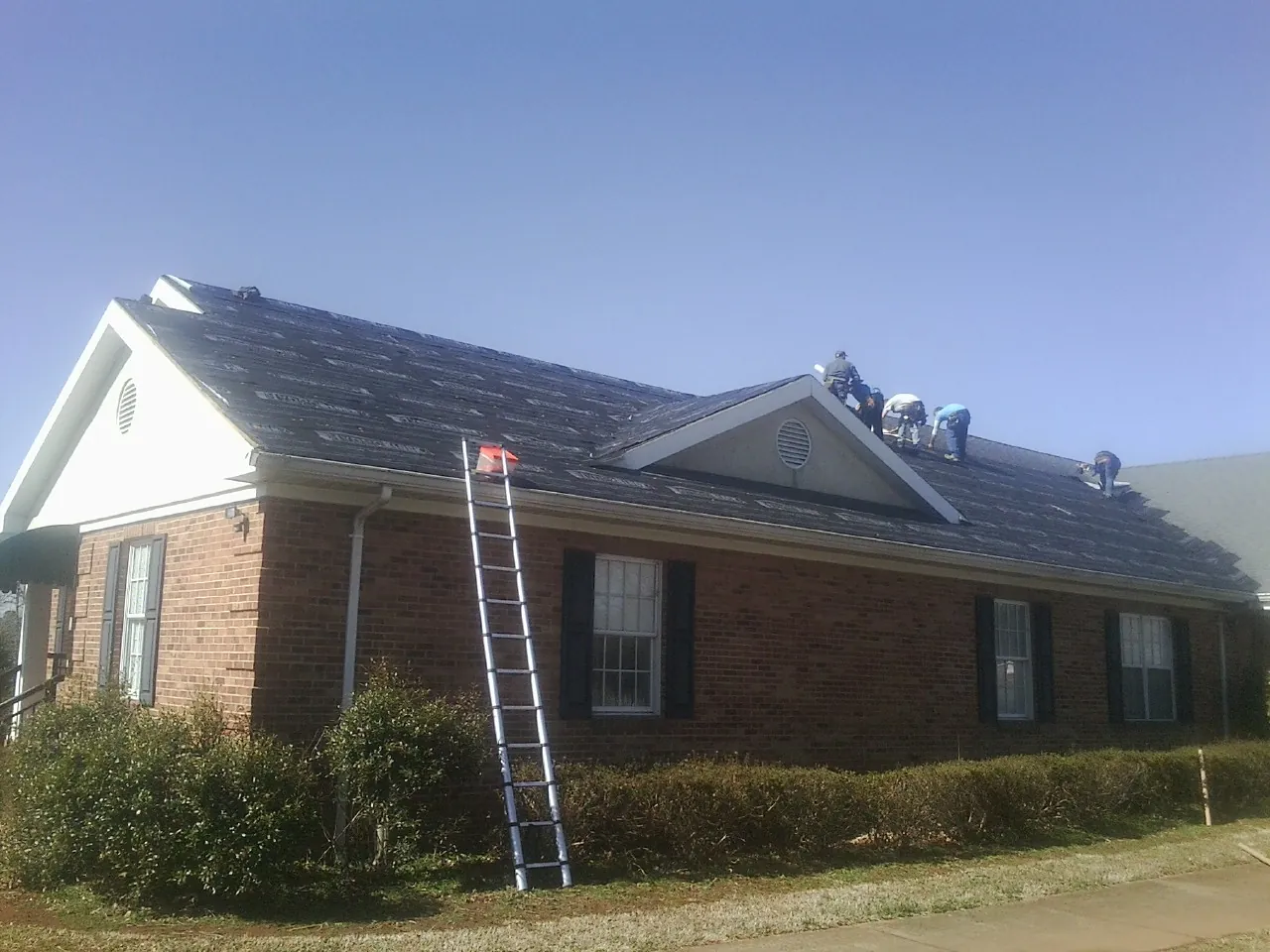 Crew tearing shingles off a brick ranch roof with a ladder set — Metal Roof Repair work by our crew in Lake Zurich