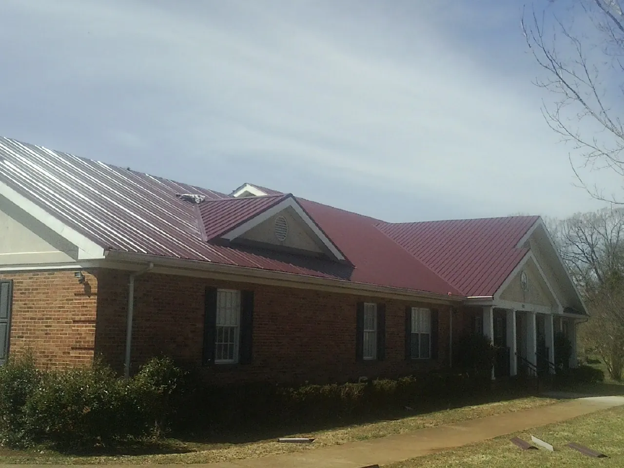 Red metal roof with gabled entries on a long brick building, from a Hail Damage Roof Repair job in Lake Zurich