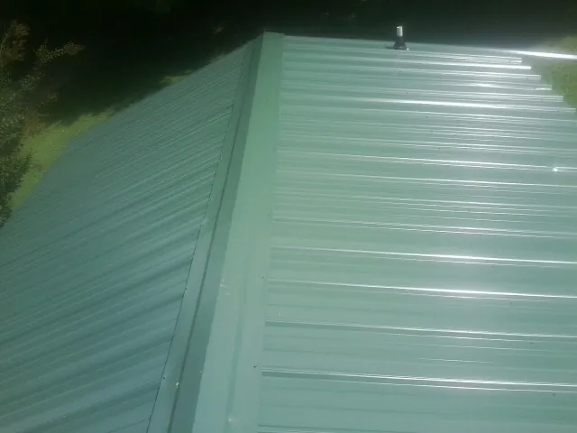 New green metal panels meeting at the ridge of a roof — Flat Roof Repair work by our crew in Lake Zurich