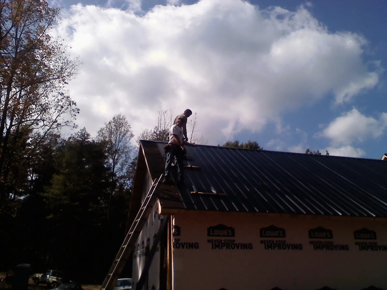 Roofer fastening dark metal panels high against a cloudy sky, from a Roof Inspection job in Lake Zurich