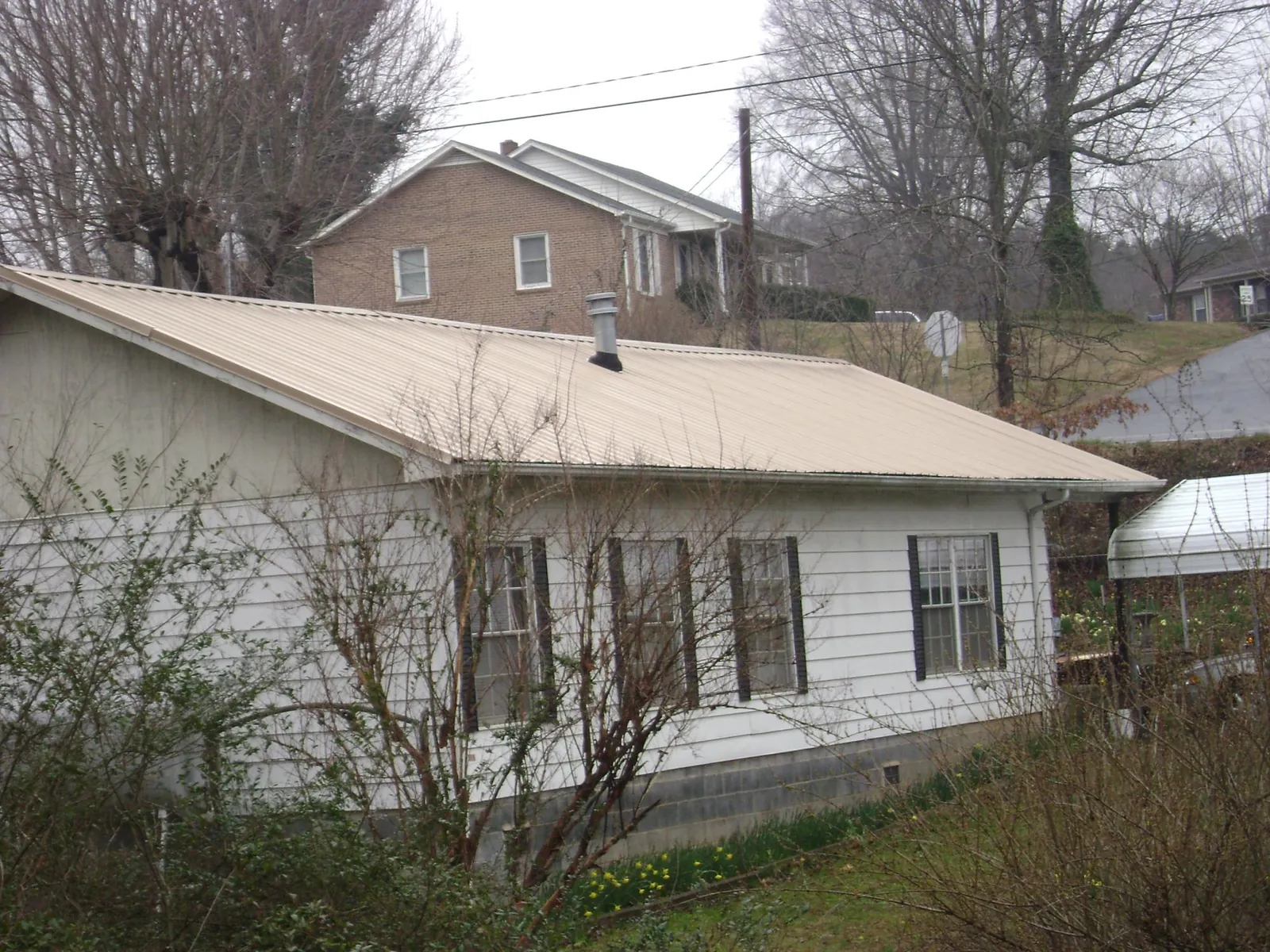 Tan metal roof on a white sided house set into a hillside — Commercial Roofing by Roofing Brothers in Lake Zurich
